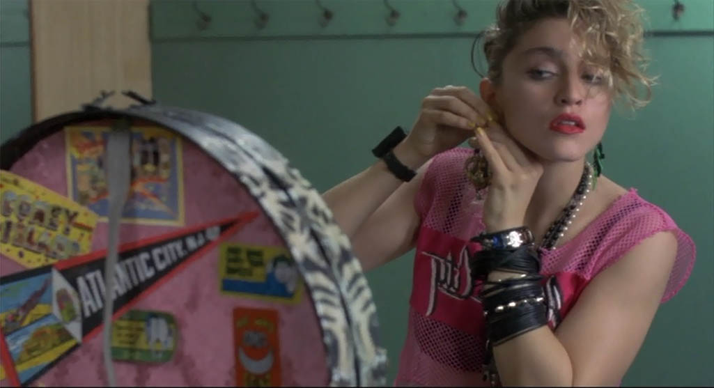 Madonna putting one of the Nefertiti earrings wearing rubber bracelets and rosaries in 'Desperately Seeking Susan.'